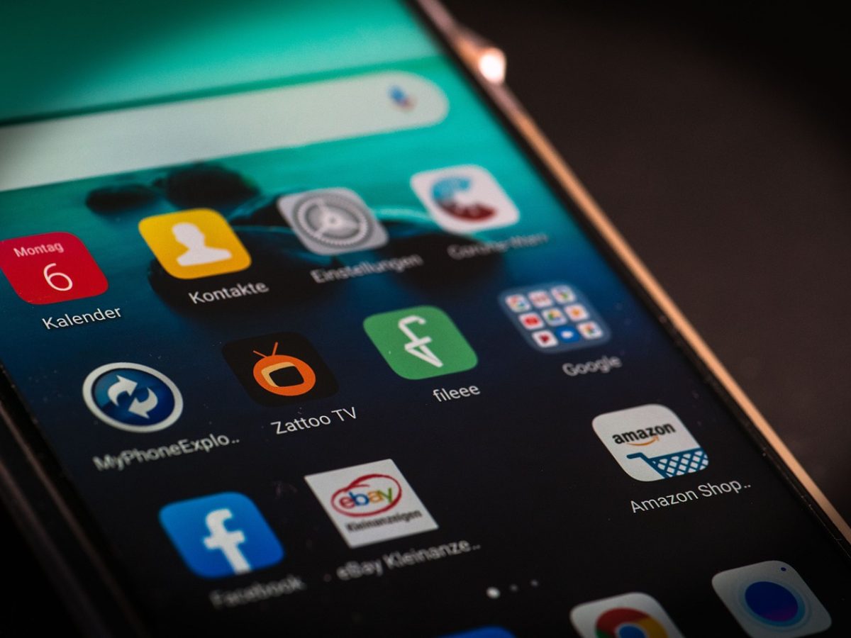 e站下载 App 主界面在手机屏幕上展示栏目导航与内容卡片，暖色灯光下手机斜放在木质桌面上，旁边放着笔记本与咖啡杯